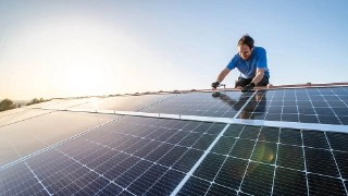 Mann installiert auf einem Dach eines Eigenheims eine Photovoltaikanlage. 